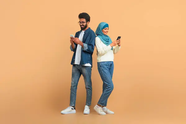Nowoczesna Para Muzułmanów Arabskich Smartfonami Stojącymi Beżowym Tle Szczęśliwy Młody — Zdjęcie stockowe