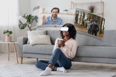 VR gözlükleri genç Afrikalı Amerikalı kadını sanal video çağrıları dünyasına taşıyor, sanal ekranda ev iletişimini yeniden tanımlıyor.
