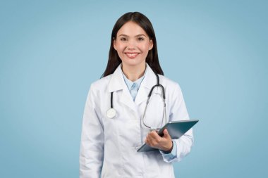 Dijital tablet tutan ve gülümseyen, rahatlatıcı mavi arka plana karşı tele-sağlık hizmetlerine hazır, yaklaşabilen kadın doktor.