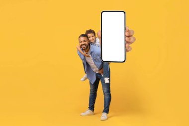 Gülümseyen Genç Siyah Baba ve Genç Oğul kamerada boş beyaz ekranlı akıllı telefon gösterisi, mutlu baba ve ergen erkek çocuğun yeni mobil uygulamayı kucaklaması ve önermesi, kopyalama alanı,