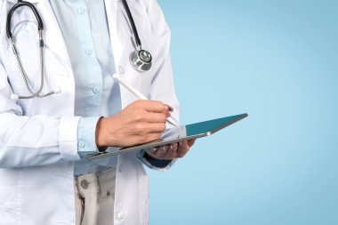 Dijital tablete yazı yazan, modern tıbbi kayıtları gösteren, steteskoplu, mavi arka planlı kadın doktorların yakın plan görüntüleri.