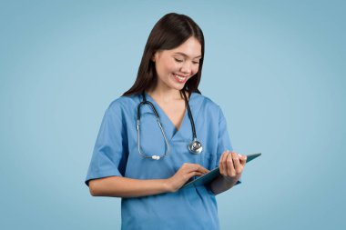 Mavi üniformalı gülümseyen hemşire, modern sağlık hizmetlerini ve tıbbi teknolojiyi sembolize eden dijital tablet kullanıyor.