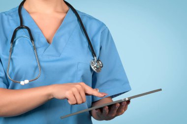Kadın hemşirelerin dijital tablet dokunmatik pedi üzerinde çalışırken, mavi arka plan üzerinde çalışırken, sağlık hizmetlerinde teknolojiyi ön plana çıkarırken, ücretsiz alan