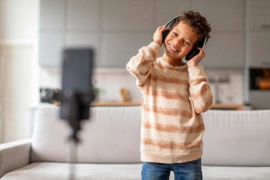 Kulaklık takan, akıllı telefon kamerasının önünde dans eden, müzik dinleyen ya da evdeki interaktif medyaya bağlanan mutlu Afrikalı Amerikalı erkek çocuk.