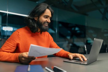 Milenyum sakallı, uzun saçlı, günlük kıyafet yöneticisi gibi giyinen, masa başında oturan, elinde evrak tutan bilgisayar kullanan, kopyalama alanı kullanan bir Hintli. Kariyer, iş