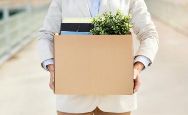 Ofis malzemeleri ve yeşil bir fabrikayla dolu bir karton kutuyu elinde tutan kişi muhtemelen iş değişikliğini ya da iş yerinde yeni bir başlangıcı işaret ediyor.