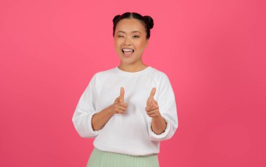 Yakaladım seni. Gülen Asyalı kadın göz kırpıyor ve işaret parmağını kameraya doğrultuyor, birini işaret ediyor, pozitif Koreli kadın pembe stüdyo arka planında yalnızken eğleniyor,