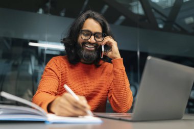 Modern ofiste çalışan, bilgisayar kullanan, telefonla konuşan, not defterine notlar alan, uzay kopyası alan, modern ofis çalışanları ve gözlük takan binlerce yıllık Hintli adam.