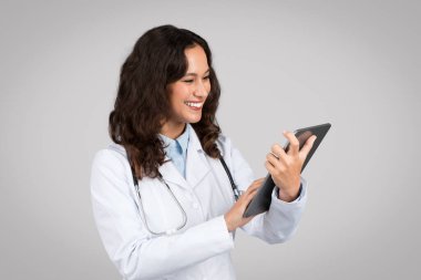 Beyaz önlüklü kadın doktor, dijital tablet kullanıyor. Sağlık hizmetlerinde modern tıbbi teknolojinin kullanıldığını gösteriyor.