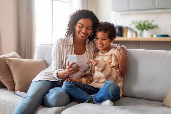 快乐的非洲裔美国人妈妈和小儿子在家里用智能手机放松一下 快乐的黑人妈妈和男孩在网上浏览 或者在沙发上休息时在线观看视频 复制空间 — 图库照片