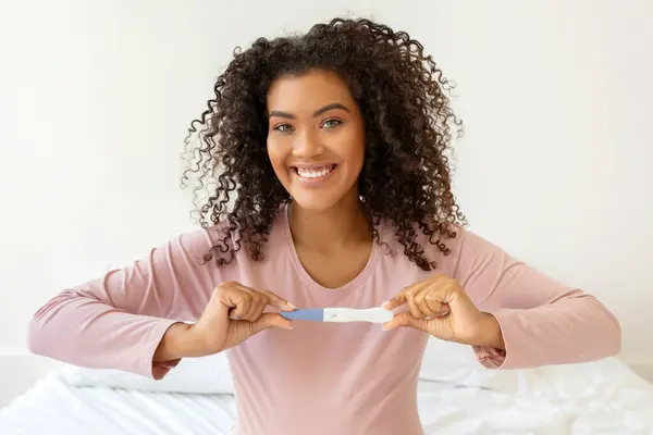 Šťastná Krásná Černoška Drží Pozitivní Těhotenský Test Při Sezení Posteli — Stock fotografie