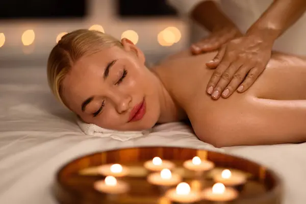 Spa Treatment. Attractive Blonde Lady Enjoying Back and Shoulders Massage In Luxury Beauty Salon, Therapist Woman Massaging Body Of Relaxed Client Indoors. Wellness Day Concept