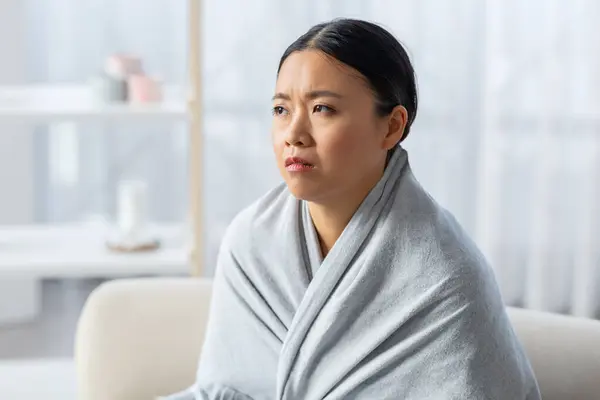 抑圧された欲求不満の若いアジアの女性は 自宅のソファーに座ってコピースペースを見ている毛布に包まれました 寒い中国の女性は冬の間に熱なしでアパートで凍結 — ストック写真