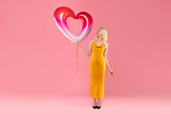 Wdzięczna Blondynka Eleganckiej Żółtej Sukni Patrząc Czerwony Biały Balon Serca — Zdjęcie stockowe