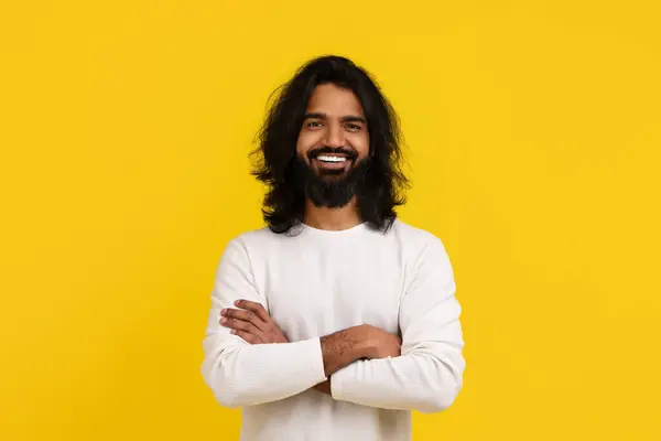 古板而又英俊的长胡子印度年轻人 身穿白色衣服 在黄色的工作室背景下显得孤立无援 双手交叉放在胸前 对着相机微笑 复制空间 — 图库照片