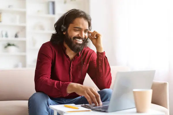 ポジティブなひげ付きミレニアルインド人男性は 自宅で働く同僚とのオンライン会議を持っています ソファーに座っている東部の男リモート従業員 ヘッドセットとコンピュータのラップトップを使用して スペースをコピー — ストック写真