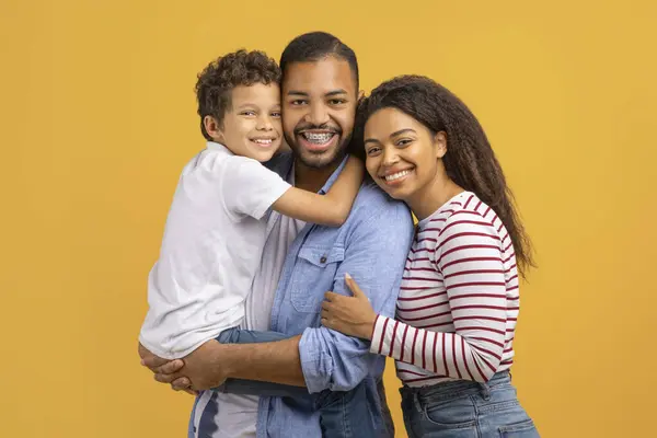 3人の幸せなアフリカ系アメリカ人の家族の肖像画は 一緒に抱擁する息子 楽しい黒人の両親と彼らの男性の子供は 黄色い背景の上に隔離され コピースペース — ストック写真