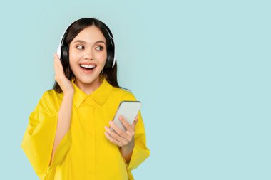 Neşeli gülümseyen, güzel, İspanyol, esmer bir kadın elinde akıllı telefonuyla kablosuz kulaklıklara dokunuyor ve fotokopi alanına bakıyor.