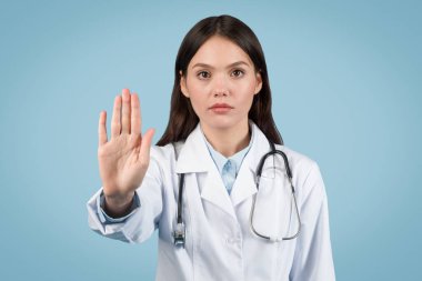 Boynuna steteskop dolamış ciddi bir kadın doktor. Durma hareketi yapıyor. Mavi arka planda dikkat ya da reddi gösteriyor.