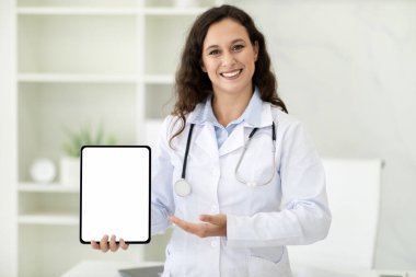 Doktorla online randevu, tele sağlık, uzaktan ilaç konsepti. Genç Avrupalı kadın doktor ellerinde, klinik hastanesinin iç kısmında beyaz beyaz ekran maketi olan dijital tablet.
