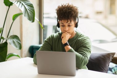 Ciddi milenyum siyahi adam serbest yazar ya da kafede bilgisayarla çalışan, kulaklık kullanan, iş arkadaşlarıyla online görüşme yapan, bilgisayar ekranına bakan, uzayı kopyalayan