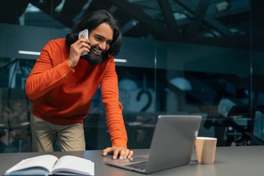 Modern ofiste çalışan, telefonla konuşan ve bilgisayar ekranına bakan günlük kıyafet proje yöneticisi gibi giyinmiş bir Hintli. Çoklu görev kavramı