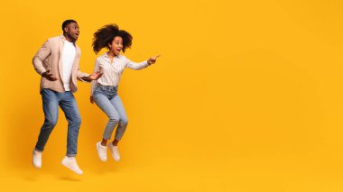 Neşeli Afrikalı Amerikalı çift, coşkuyla, canlı, hareketli bir atmosfer yaratarak, canlı sarı arka planda özgürlüklerini ve mutluluklarını ifade ederek, dinamik bir atlayışla yakalandılar.