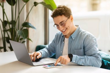 Gözlüklü mutlu genç Avrupalı öğrenci, akıllı telefon, dizüstü bilgisayar, iş, internet üzerinden çalışma, kafede sohbet. Çevrimiçi toplantı uygulaması, modern yaşam tarzı uzaktan, dijital göçebe