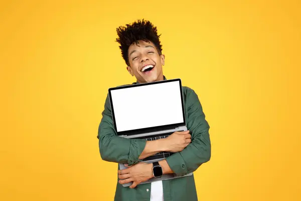 欣喜若狂的黑人年轻人抱着电脑笔记本电脑 用白色的空白屏幕 享受着他的新电脑 找到了理想的工作 庆祝网上销售 黄色背景 复制空间 — 图库照片