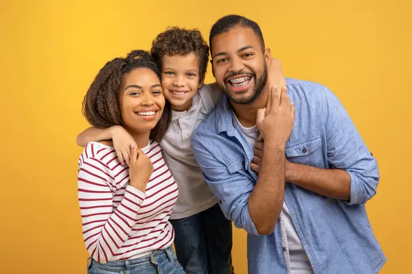 3人の幸せなアフリカ系アメリカ人家族で 黄色いスタジオの背景 黒人の両親と男性の子供に愛とトータルを表現しながら お互いに暖かく抱擁しています — ストック写真
