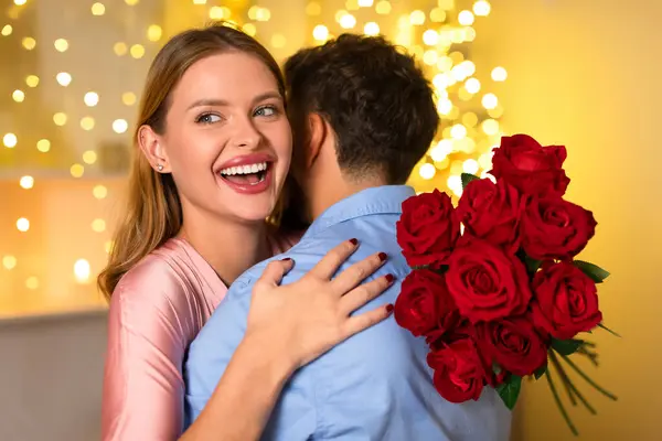 一个容光焕发的女人 笑容满面地拥抱着男人 背着一束红玫瑰 在喜庆的气氛中喜形于色 — 图库照片