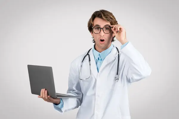 Shocked Male Doctor Adjusting His Glasses Holding Laptop Perplexed Expression Royalty Free Stock Images