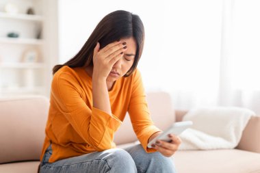 Bin yıllık üzgün Çinli kadın elinde akıllı telefonuyla koltukta oturuyor, yüzüne dokunuyor, yıkıcı bir mesaj alıyor, internetten haberleri okuyor, ev içini okuyor, uzay kopyaları yapıyor.