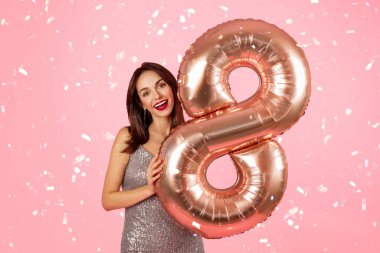 Bin yıllık Kafkasyalı, elinde 8 balon olan esmer bir kadının pembe arka planda, stüdyoda izole edilmiş konfetiyle eğlenmesine sevindim. Yaşam tarzı kutlaması, tatil ve eğlence