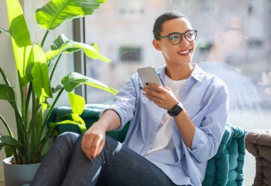 Gözlüklü neşeli genç latin bayan, huzur ve boş zamanın tadını çıkar, cep telefonuyla yazı yaz, modern kafede sosyal ağlarda sohbet et, ofis içinde. Rahatla, aygıt üzerine blog, reklam ve teklif