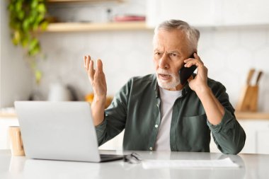 Cep telefonuyla konuşan ve mutfakta dizüstü bilgisayar kullanan stresli yaşlı beyefendi, müşteri desteği ile konuşan, bilgisayar ya da internetle sorunları olan yaşlı beyefendi,