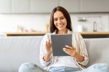 Dijital tabletle koltukta dinlenen gülümseyen güzel bir kadının portresi, internette gezen mutlu bir kadın ya da internetten alışveriş yapan, evinde bilgisayarla dinlenen, boşluğu kopyalayan...