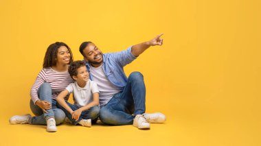 Şuna bak. Mutlu siyahi aile birlikte oturuyor ve fotokopi alanını işaret ediyor, neşeli Afro-Amerikan anne ve baba ve oğlu faiziyle bedava bir yere bakıyor, sarı stüdyo arka planında poz veriyorlar, panorama