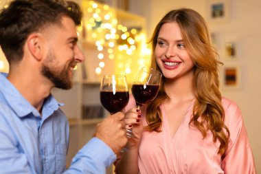 Kırmızı şarap kadehleriyle neşeli genç bir çift, sıcak, neşeli peri ışıklarına karşı mutluluk anlarını paylaşıyorlar.