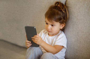 Akıllı telefon kullanan, evdeki kanepede oturan, küçük tatlı anaokulu öğrencisi kız çocuk mobil oyunlar oynuyor ya da internetten çizgi film seyrediyor, fotokopi odasıyla yakın çekim yapıyor.