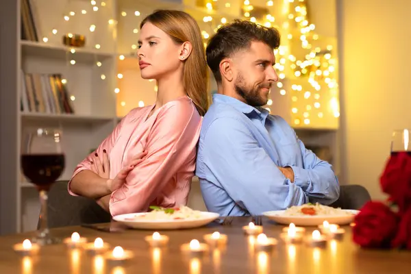 ヨーロッパのカップルは 柔らかい照明とロマンチックな夕食の背景に対して 腕で後ろに座って紛争の兆候を示しています — ストック写真