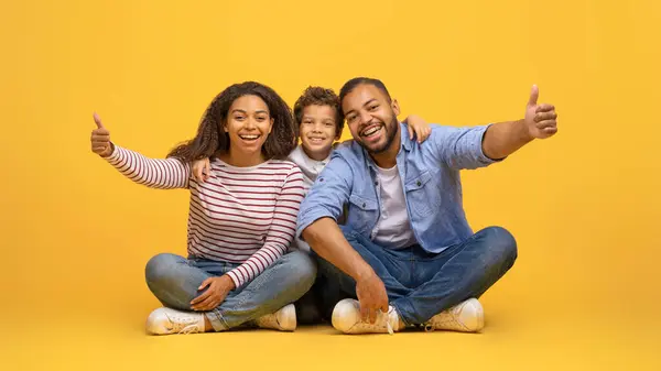概念のように 3人の幸せなアフリカ系アメリカ人の家族は スタジオで黄色い背景に座っている間 ハッピーブラックの両親と小さな息子が承認または推薦 スペースをコピー — ストック写真