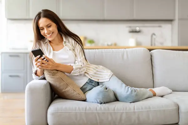 Contentada Fêmea Gostando Navegar Seu Smartphone Enquanto Senta Sofá Acolhedora — Fotografia de Stock