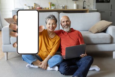 Evde dizüstü bilgisayarla dinlenirken kamerada boş akıllı telefon gösteren, gülümseyen yaşlı eşler Yeni Mobil Uygulama veya Web Sitesi, Yaratıcı Kolaj,