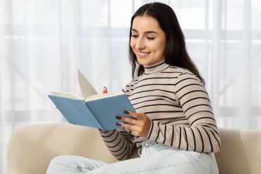 Neşeli, sakin, bin yıllık Kafkasyalı kadın kitap okuyor, planlama günü, çalışıyor, kanepeye oturuyor, oturma odasının iç tarafında. Evde rahat öğrenim, eğitim, hobi ve edebiyat hayatı