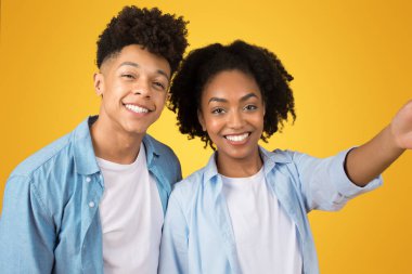 Mutlu, Afro-Amerikan erkek ve bayan, günlük çekimlerde, video görüşmesinde, turuncu arka plandaki stüdyoda izole edilmiş, kapatın. Sosyal ağlar için fotoğraf, blog yazarları videosu, öğrenci toplantısı