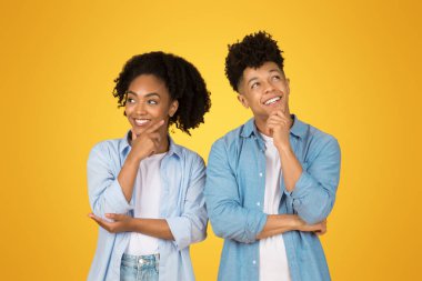 Gülümseyen genç Afro-Amerikalı erkek ve kadın gündelik düşünceler içinde, boş alana bakın, turuncu arka plan stüdyosunda izole edilmiş. Pozitif yaşam tarzı, soru, seçim birlikte, satış