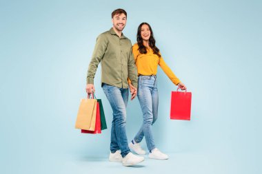 Mutlu adam ve kadın günlük yürüyüşler, renkli alışveriş torbaları, ferahlatıcı mavi arka planda birlikte alışverişin tadını çıkarıyorlar.