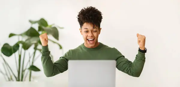Excited millennial african american guy businessman celebrating success, working at home officw, looking at laptop computer screen and clenching fists, got great news, panorama. Business success