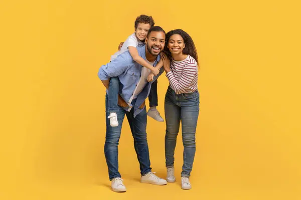 3人の幸せな黒人家族の全長ショット スタジオで黄色の背景で一緒に楽しんだ息子と 喜びの瞬間を共有するアフリカ系アメリカ人の両親と男性の子供を微笑み 喜びをコピースペース — ストック写真